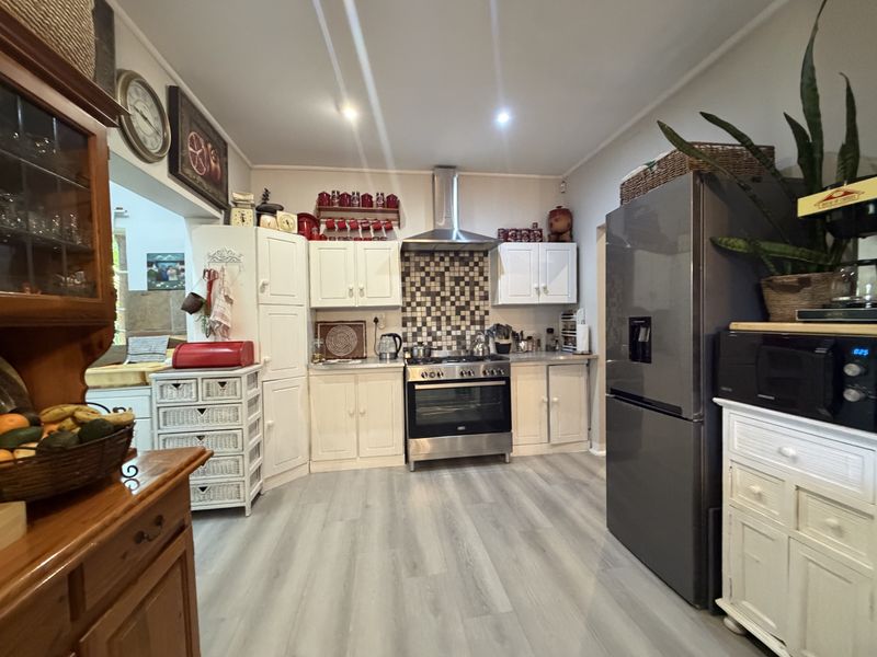 A functional kitchen featuring white cabinetry, a stainless steel oven with extractor fan, mosaic tile splashback, and modern laminate flooring.