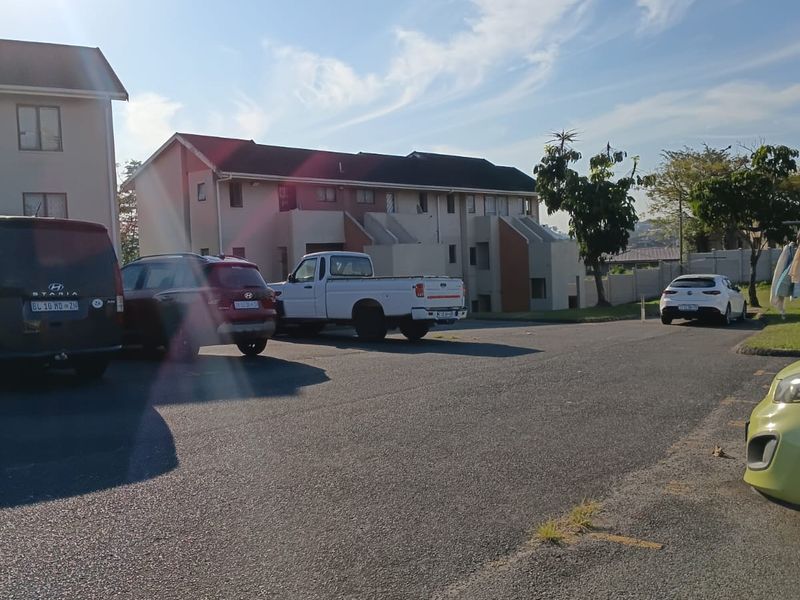 Exterior view of a multi-story apartment complex featuring an asphalt parking area and external staircases.