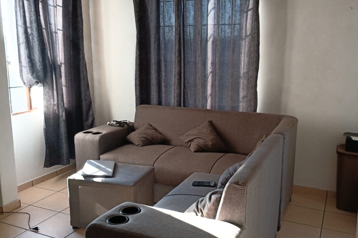 A living room area featuring ceramic floor tiles and natural light from windows with curtains.