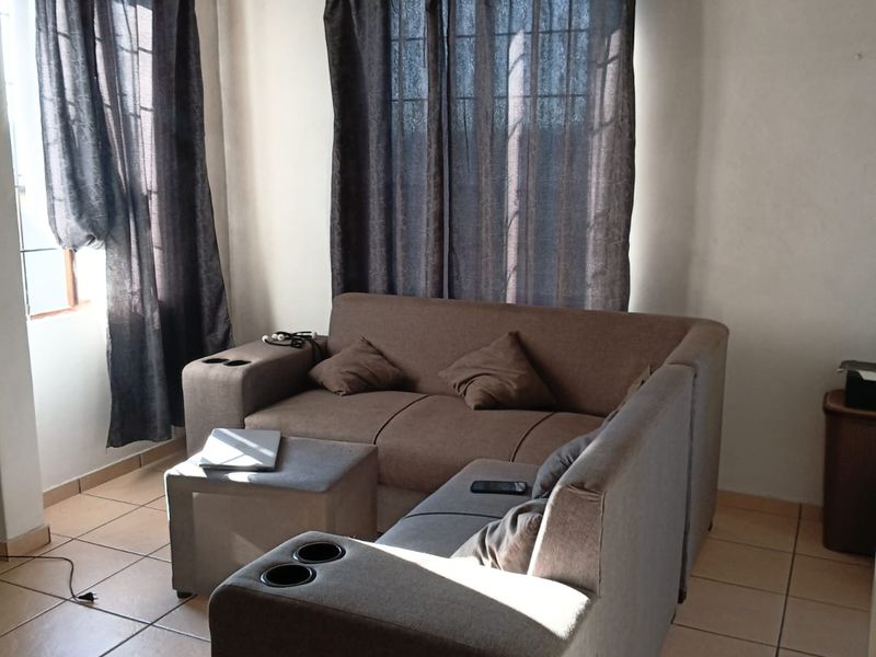 A living room area featuring ceramic floor tiles and natural light from windows with curtains.