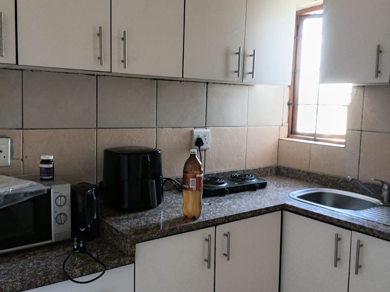 Compact kitchen featuring white cabinetry, granite countertops, tiled backsplash, and a stainless steel sink, providing a functional workspace.