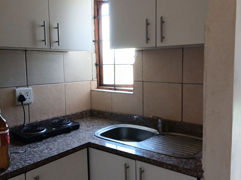 Compact kitchen featuring white cabinetry, laminate countertops, a stainless steel sink, and tiled backsplash with a window providing natural light.