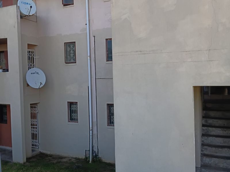 Rear elevation of an apartment building showing exterior stairwell access, security gates, and satellite dish installations on weathered plastered walls.