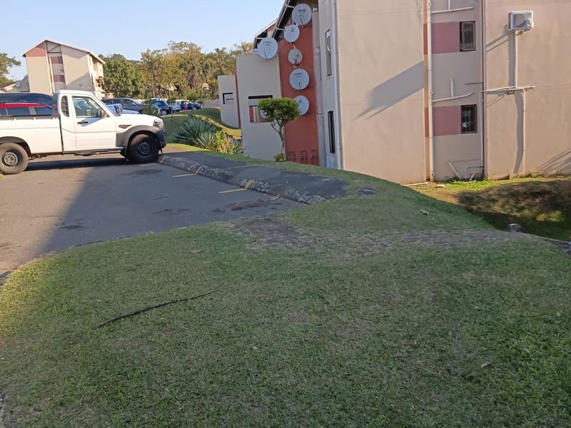 Exterior view of the apartment building showing the rear facade, paved parking area, and surrounding lawn.