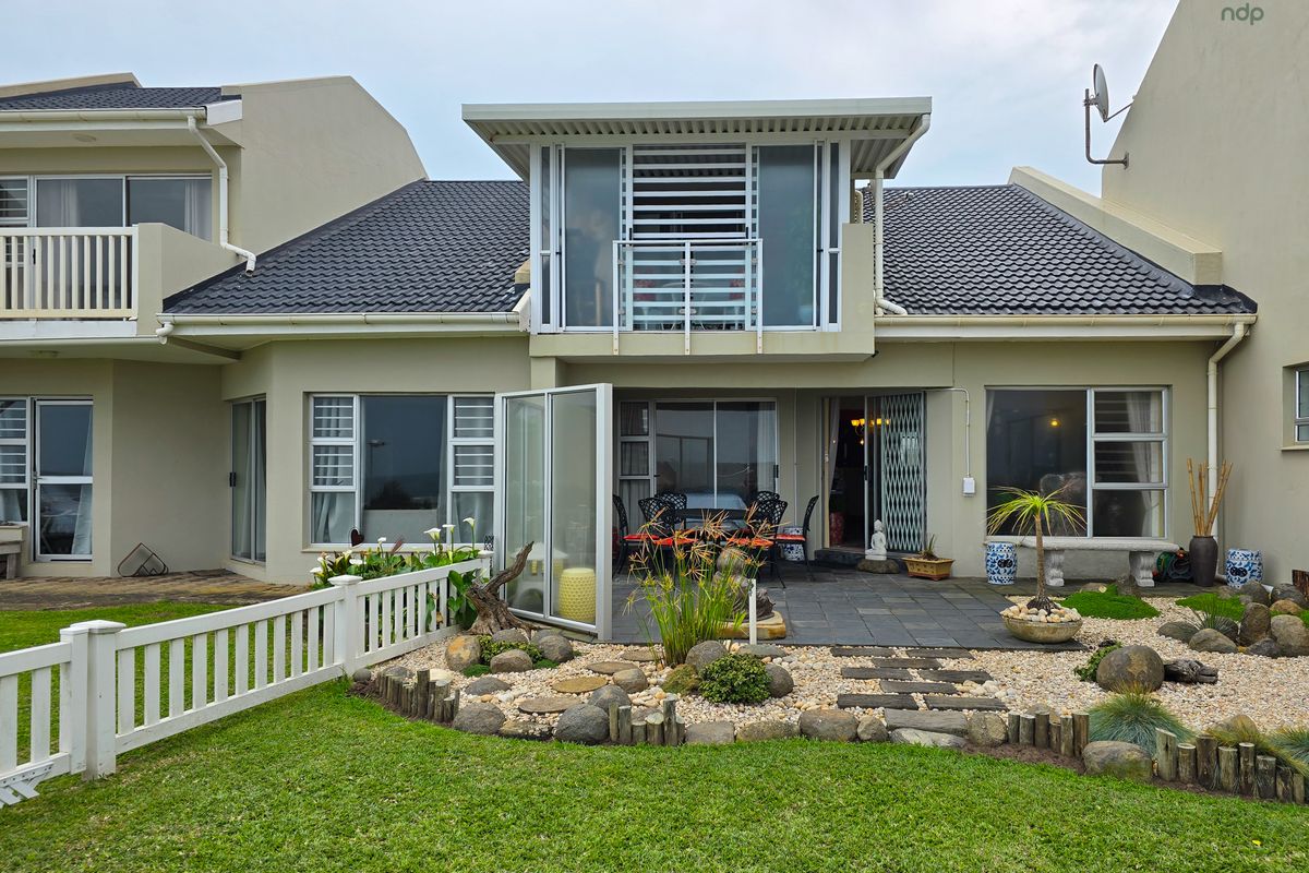 Rear view of the townhouse featuring a landscaped garden, stone-paved patio area, and an upper-level balcony with sliding glass doors.