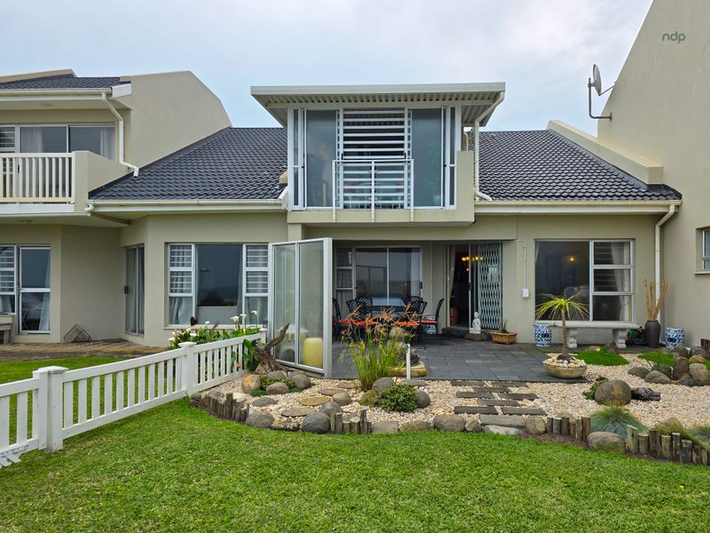 Rear view of the townhouse featuring a landscaped garden, stone-paved patio area, and an upper-level balcony with sliding glass doors.