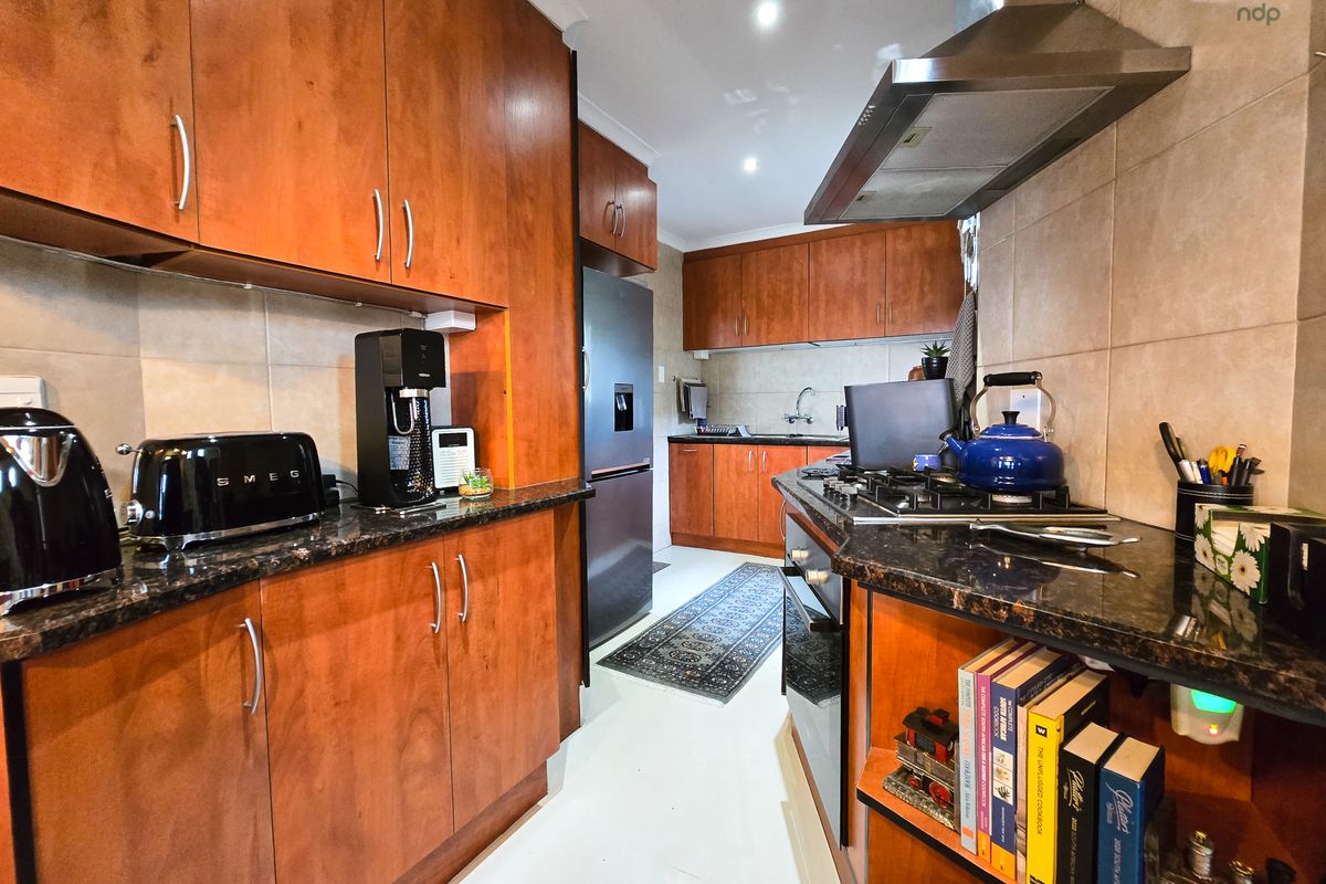 A functional kitchen featuring warm-toned wooden cabinetry, granite countertops, a gas hob with extractor fan, and a tiled backsplash.