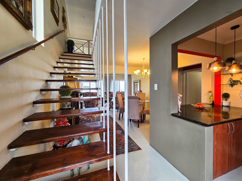 Open-plan living area featuring a striking open-tread timber staircase, granite kitchen countertops, and integrated cabinetry, creating a seamless flow between levels.