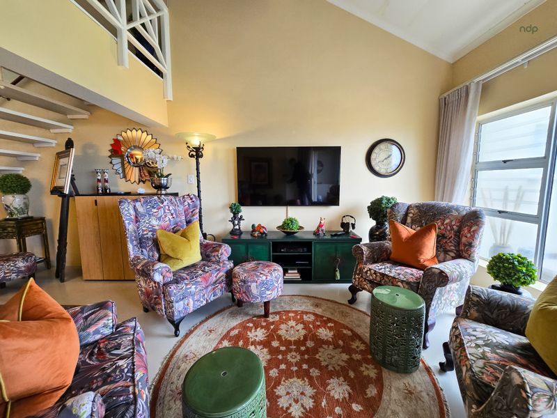 A bright living room featuring a high vaulted ceiling, an open staircase with a white railing, and large windows allowing for natural light.