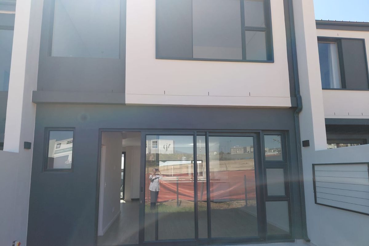 Rear elevation of a modern townhouse featuring large sliding glass doors, contemporary dark grey and cream exterior finishes, and integrated wall lighting.