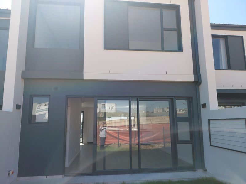 Rear elevation of a modern townhouse featuring large sliding glass doors, contemporary dark grey and cream exterior finishes, and integrated wall lighting.