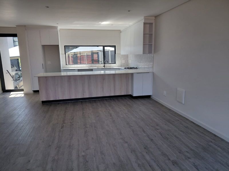 Modern open-plan kitchen featuring a breakfast island, sleek white cabinetry, gas hob, and durable laminate flooring in a bright, contemporary living space.