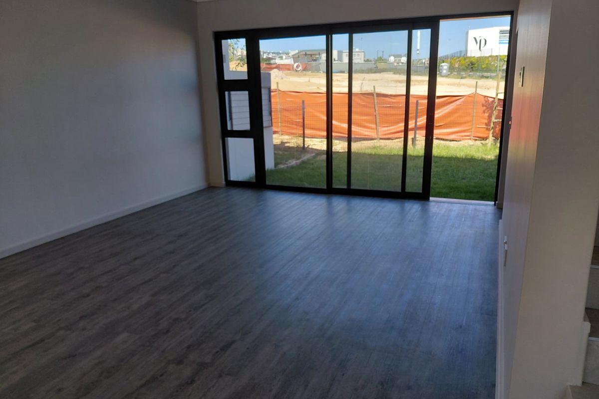 A bright, empty living room featuring modern laminate flooring, a ceiling fan, and large sliding glass doors that open to a rear garden area.