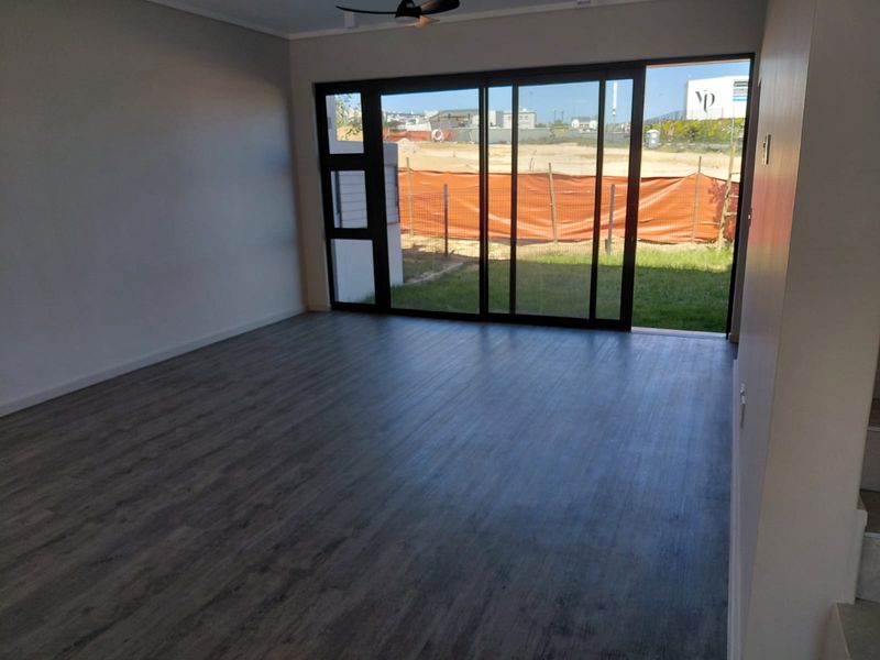 A bright, empty living room featuring modern laminate flooring, a ceiling fan, and large sliding glass doors that open to a rear garden area.