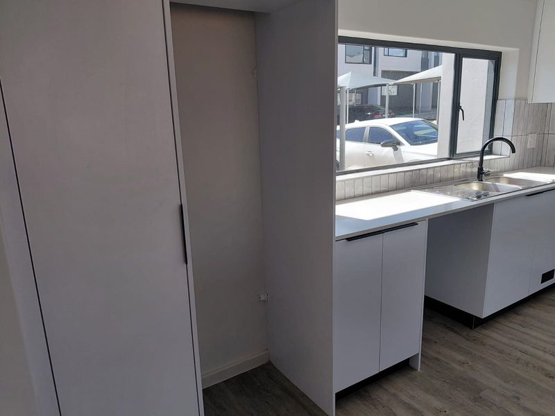 A clean, modern kitchen area featuring white cabinetry, a stainless steel sink with mixer tap, tiled splashback, and wood-look laminate flooring.