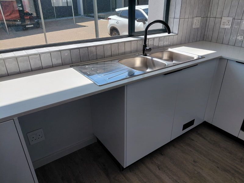 Modern kitchen area featuring white cabinetry, quartz countertops, a double bowl stainless steel sink with a black mixer tap, and subway tile backsplash.