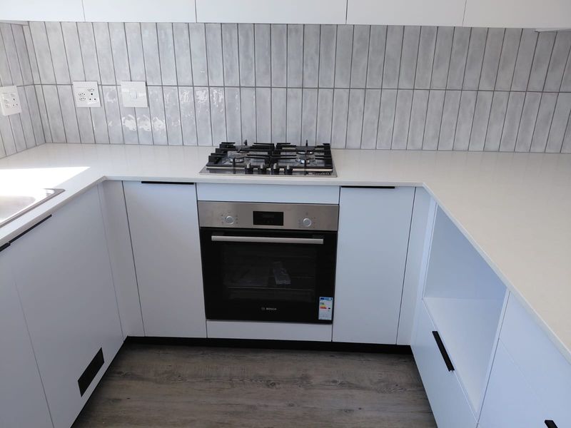 Modern kitchen featuring white cabinetry, quartz countertops, a gas hob, and a built-in oven with a stylish grey subway tile backsplash.