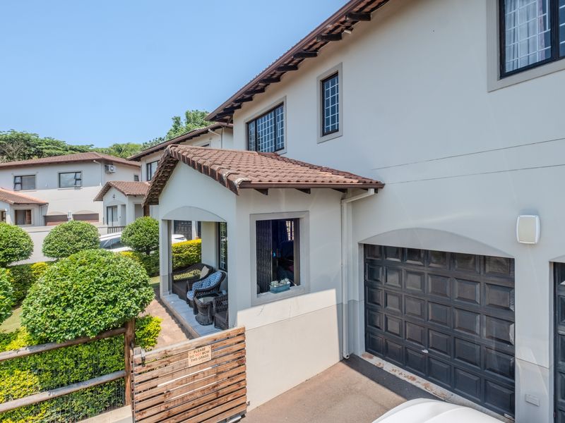 Front elevation of a townhouse featuring a double garage, covered patio area, and well-maintained exterior finishes with landscaped garden surroundings.