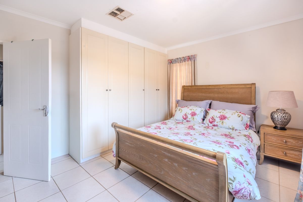 A well-maintained bedroom featuring neutral tiled flooring, built-in cupboards, and a ducted air conditioning vent.