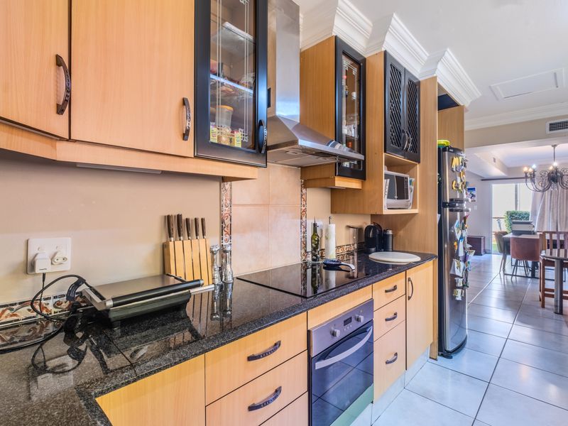 A well-maintained kitchen featuring granite countertops, built-in cabinetry, an electric hob, and a stainless steel extractor fan, flowing into an open-plan dining area.