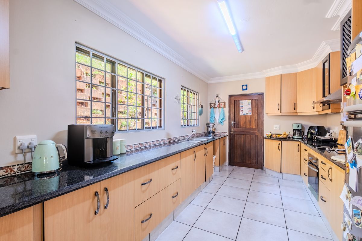 A functional kitchen featuring light wood cabinetry, granite countertops, a decorative tile backsplash, and tiled flooring with ample natural light from large windows.