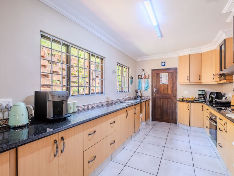 A functional kitchen featuring light wood cabinetry, granite countertops, a decorative tile backsplash, and tiled flooring with ample natural light from large windows.
