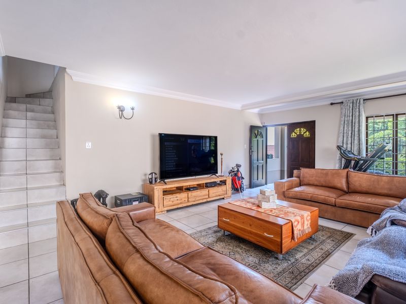 Spacious living room featuring tiled flooring, a staircase, and direct access to the exterior through a security gate.