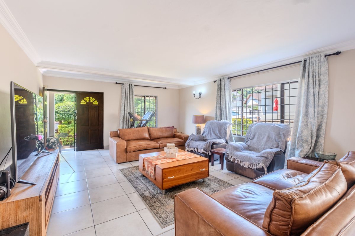 Spacious living room featuring tiled flooring, coved ceilings, and large windows with security bars, providing natural light and direct access to the garden.