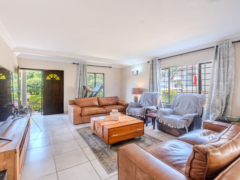 Spacious living room featuring tiled flooring, coved ceilings, and large windows with security bars, providing natural light and direct access to the garden.