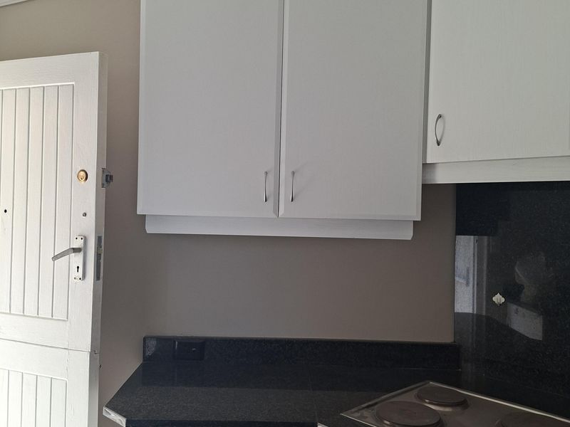 A compact kitchen featuring white cabinetry, dark granite countertops, and a built-in electric oven and hob with a stone splashback.