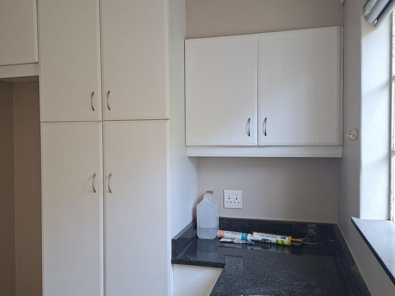A functional kitchen area featuring white built-in cabinetry, dark granite countertops, and a double bowl stainless steel sink with a modern mixer tap.