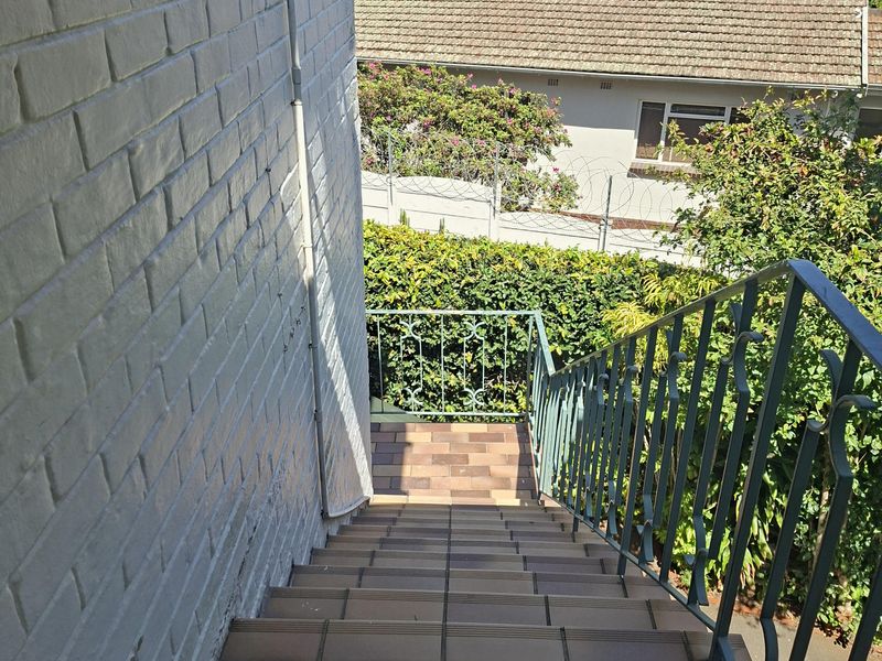 An outdoor tiled staircase with a metal balustrade leading down to a garden area, featuring a painted brick wall.