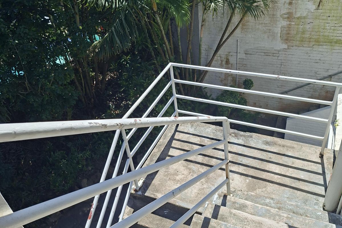 An outdoor concrete staircase with metal railings leading down to a garden area, showing signs of weathering and paint wear.