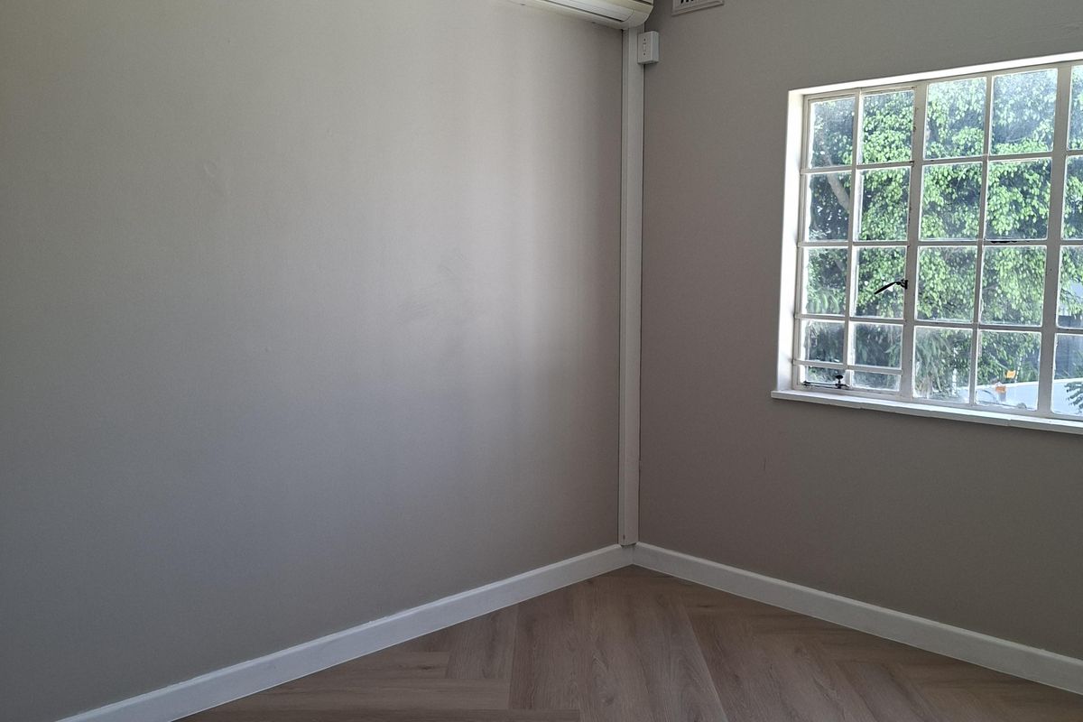 A bright, empty bedroom featuring modern herringbone flooring, neutral walls, and a wall-mounted air conditioning unit.