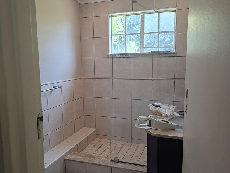 A bathroom featuring a walk-in shower with a glass screen, tiled finishes, and a vanity cabinet, currently undergoing minor finishing work.