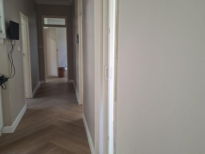 A bright hallway featuring modern herringbone flooring and neutral wall finishes, providing access to multiple rooms within the apartment.