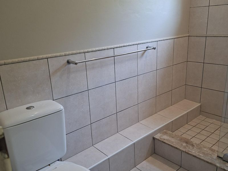 A functional bathroom featuring a toilet and a tiled shower enclosure with neutral ceramic wall and floor tiles.
