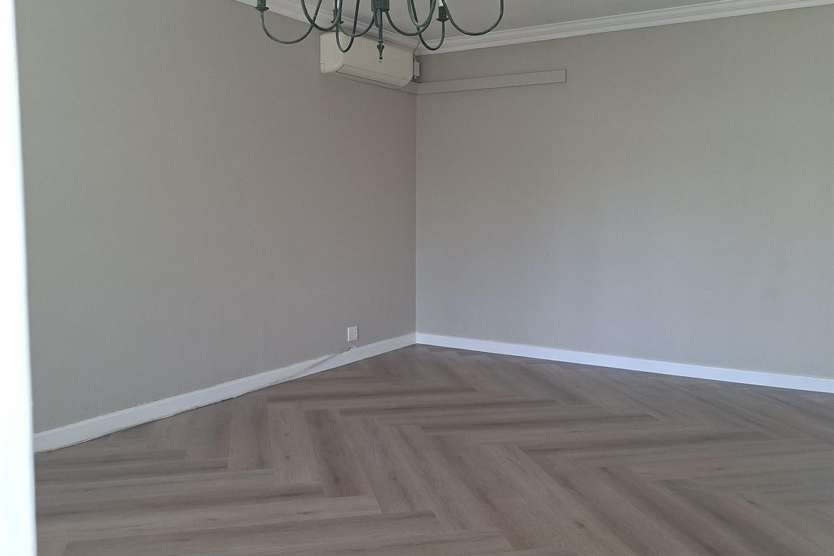 A bright, empty living room featuring modern herringbone flooring, crown molding, and a wall-mounted air conditioning unit.
