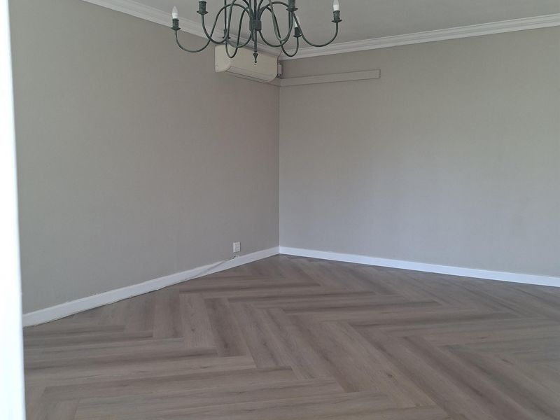 A bright, empty living room featuring modern herringbone flooring, crown molding, and a wall-mounted air conditioning unit.