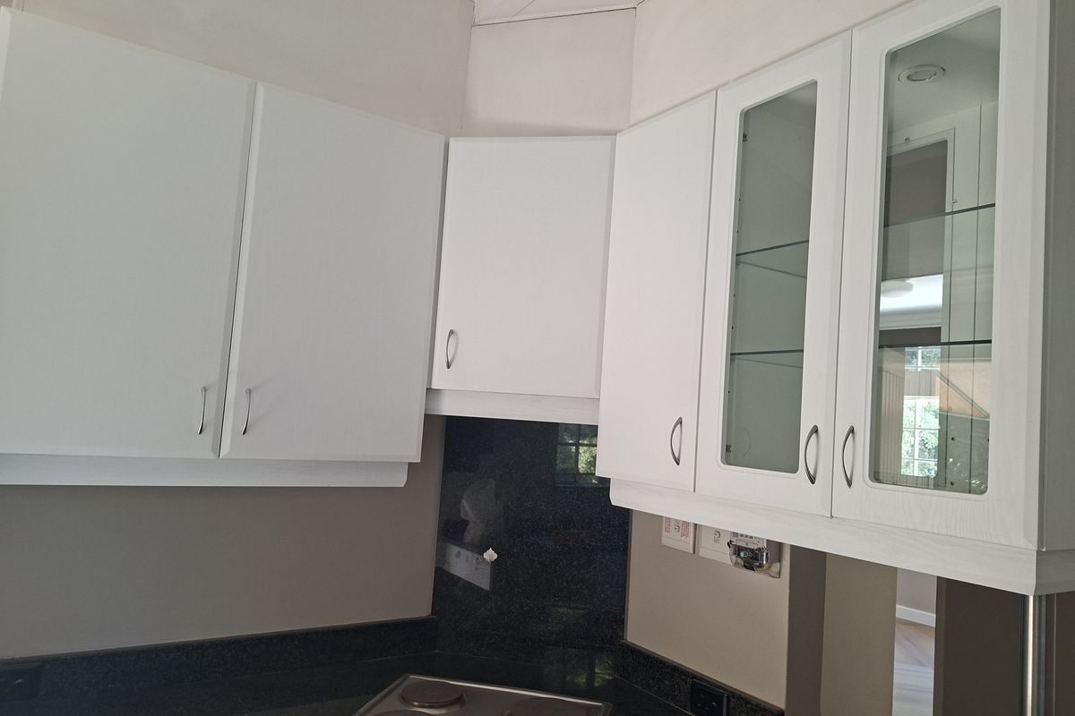 A clean kitchen area featuring white cabinetry, glass-fronted display cupboards, dark granite countertops, and a built-in electric hob.