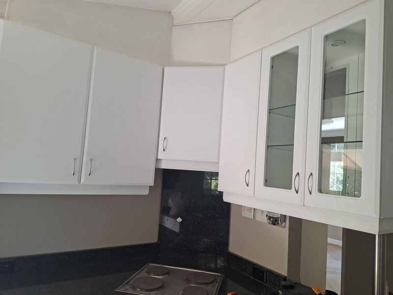 A clean kitchen area featuring white cabinetry, glass-fronted display cupboards, dark granite countertops, and a built-in electric hob.