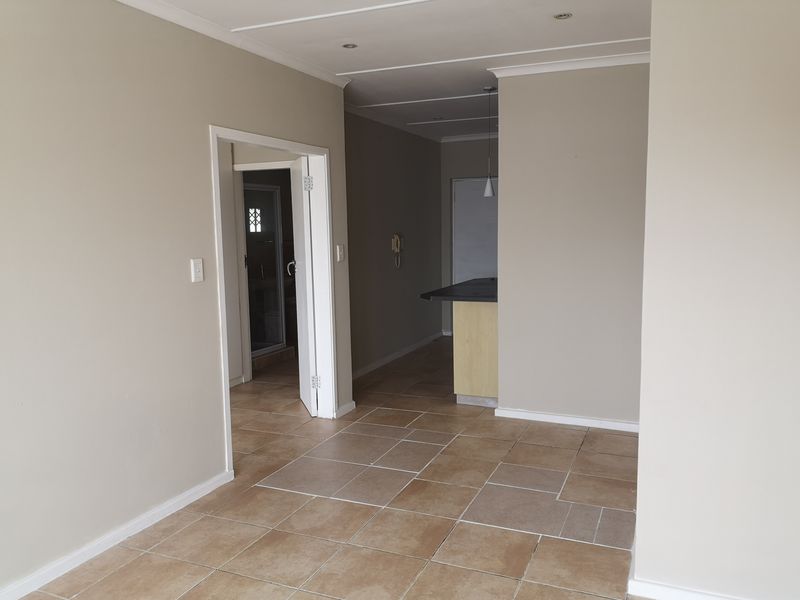 An open-plan living area featuring neutral wall tones, tiled flooring, recessed lighting, and a breakfast bar, offering a versatile space for modern living.