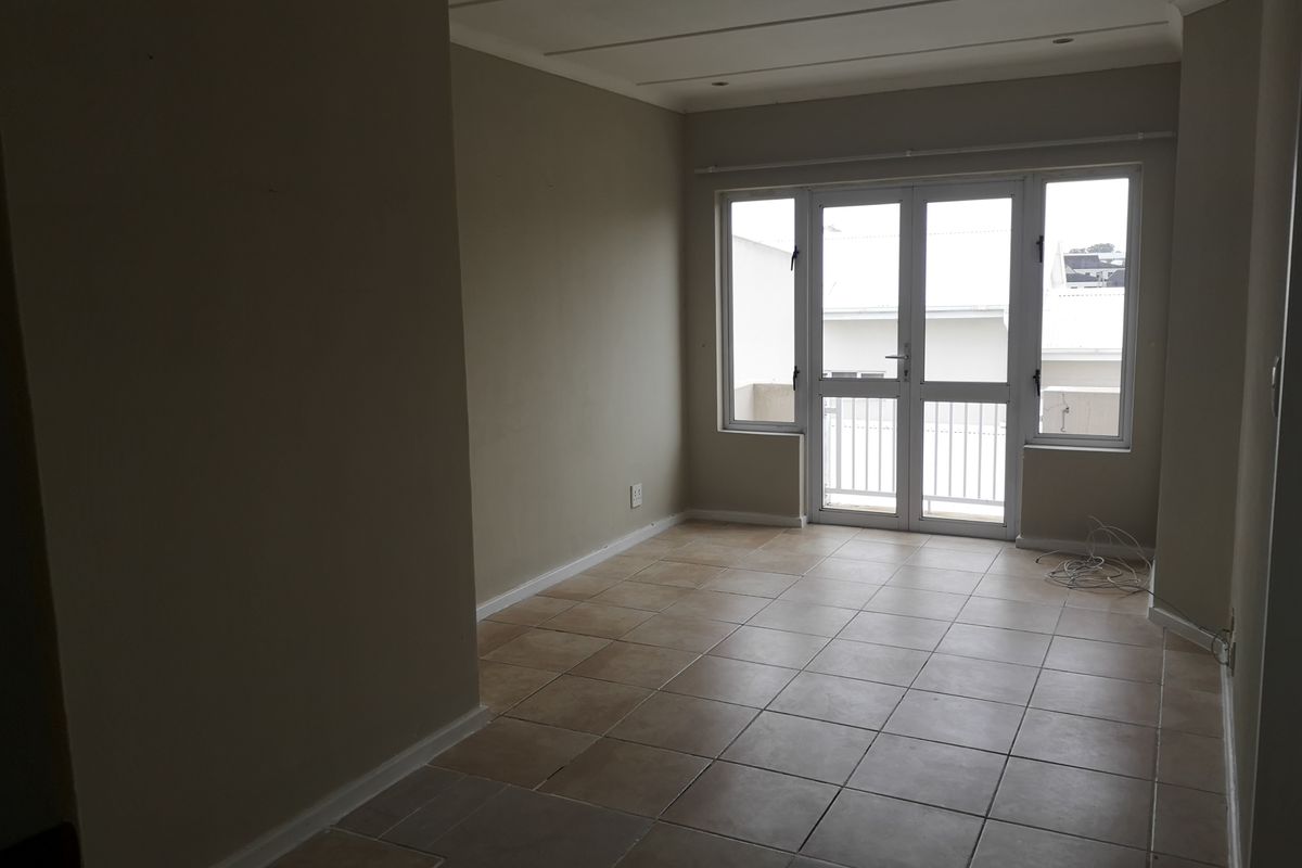 An empty, neutrally painted living area featuring tiled flooring and double glass doors leading to an outdoor space.