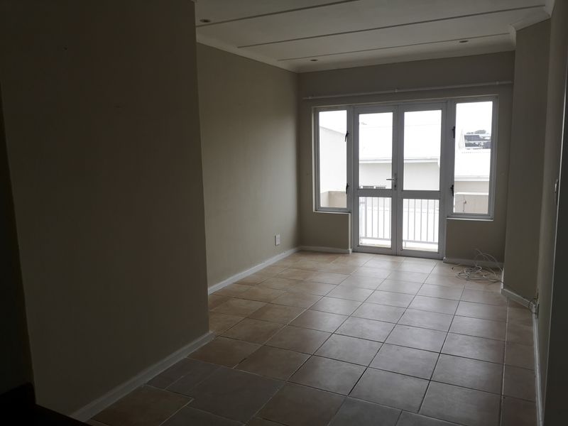 An empty, neutrally painted living area featuring tiled flooring and double glass doors leading to an outdoor space.