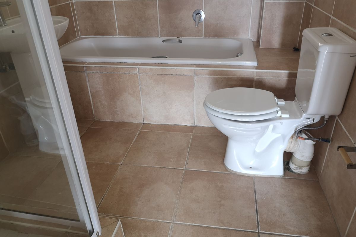 A functional bathroom featuring a built-in bathtub, pedestal sink, toilet, and a separate shower enclosure with neutral floor-to-ceiling tiling.