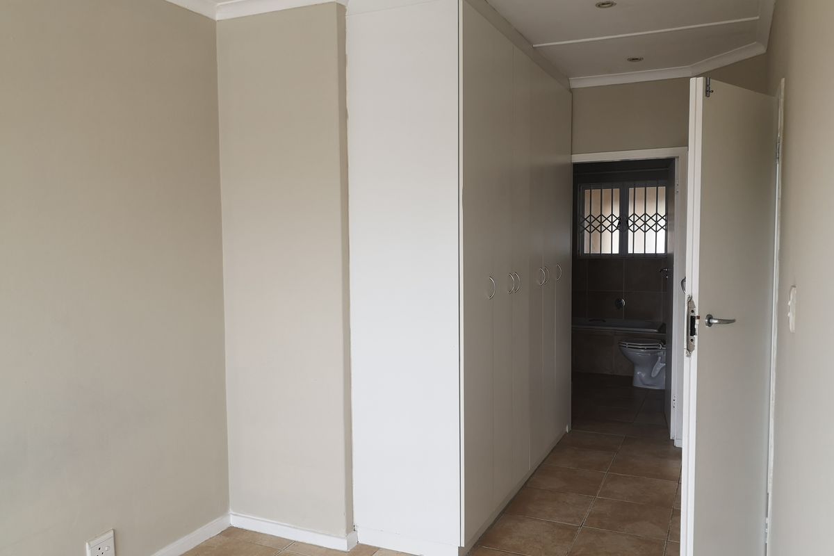 A clean, empty bedroom featuring neutral walls, tiled flooring, and ample built-in cupboard space, with an adjoining bathroom visible through the doorway.