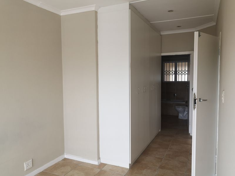A clean, empty bedroom featuring neutral walls, tiled flooring, and ample built-in cupboard space, with an adjoining bathroom visible through the doorway.