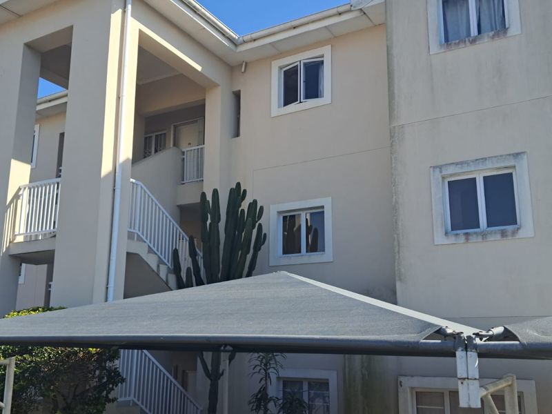 Exterior view of an apartment building facade featuring a staircase, balcony railings, and a shade sail structure.