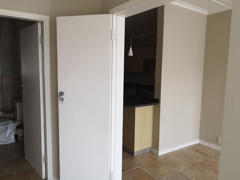 A neutral-toned hallway area featuring tiled flooring, providing access to an adjacent bathroom and kitchen space.
