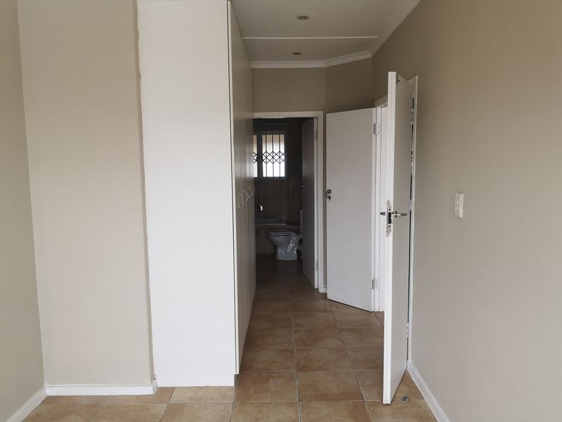 A clean, empty hallway featuring built-in cupboards, tiled flooring, and recessed lighting, providing access to an adjacent bathroom.